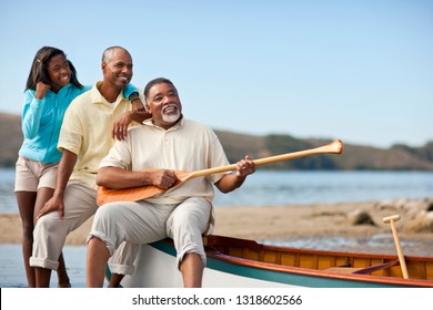 Smiling Multi Generational Family Sitting Near A Canoe On A Beach.