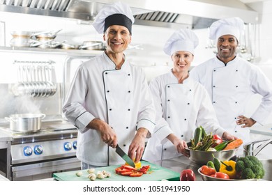 smiling multicultural chefs looking at camera at restaurant kitchen