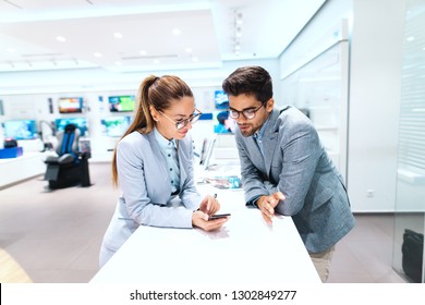 Smiling Multicultural Couple Dressed In Buying New Smart Phone. Woman Trying Out Phone. Tech Store Interior.