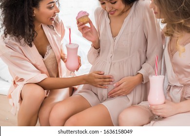 smiling multicultural girlfriends and young pregnant woman holding cupcake and glasses with milkshakes on baby shower  - Powered by Shutterstock