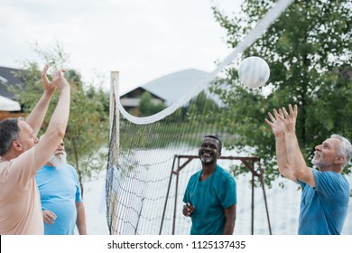 Smiling Multicultural Old Friends Playing Volleyball On Beach On Summer Day