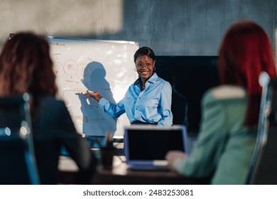 Smiling multicultural successful team leader standing at conference room and pointing at whiteboard. African american businesswoman presenting business strategy and innovative ideas to her female team - Powered by Shutterstock