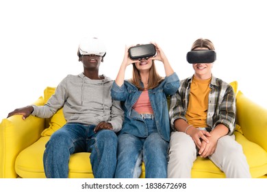 Smiling Multicultural Teenagers In Vr Headsets Sitting On Yellow Couch Isolated On White