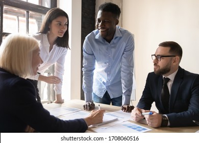 Smiling multiethnic businesspeople work together brainstorm consider paperwork at team briefing in office, happy diverse colleagues discuss financial documents share business ideas at meeting