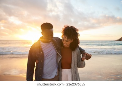 Smiling multiethnic couple walking arm in arm on a beach at sunset - Shutterstock ID 2162376355