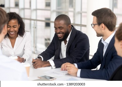 Smiling multiethnic millennial employees sit at office desk talk laugh at company boardroom meeting, happy diverse workers feel overjoyed brainstorm have fun joke at team meeting in conference room - Shutterstock ID 1389203003