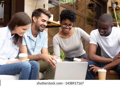 Smiling Multiethnic Millennial Friends Sit Outside In Café Look At Laptop Screen Laughing Have Fun Together, Happy Diverse Young People Rest In Coffeeshop Relax Watching Funny Video On Computer