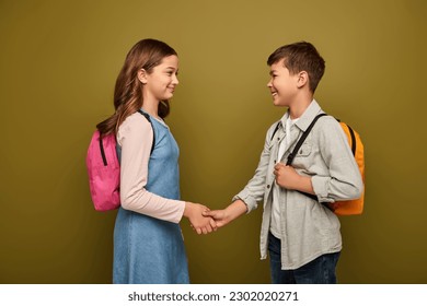 Smiling multiethnic schoolkids with backpacks shaking hands and looking at each other during international child protection day celebration on khaki background - Powered by Shutterstock