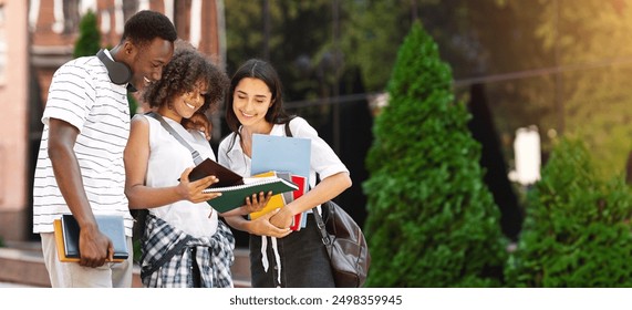 Smiling multiethnic students standing outdoors, checking college curriculum together, reading information in notebook - Powered by Shutterstock