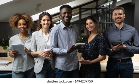Smiling multiracial business team with african male leader standing together looking at camera in office, happy international diverse employees professionals company staff group corporate portrait