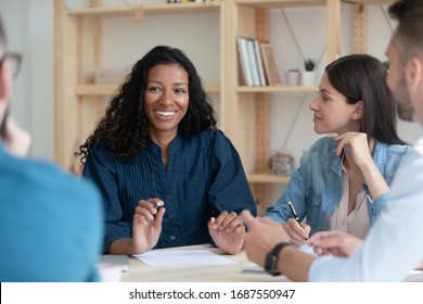 Smiling multiracial businesspeople sit at desk in office brainstorm discuss ideas together, happy diverse multiethnic colleagues coworkers talk cooperate at meeting or briefing, teamwork concept
