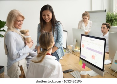 Smiling Multiracial Colleagues Of Different Age Talking In Office, Happy Friendly Asian Caucasian Female Coworkers Or Young And Senior Aged Businesswomen Having Pleasant Fun Conversation At Workplace