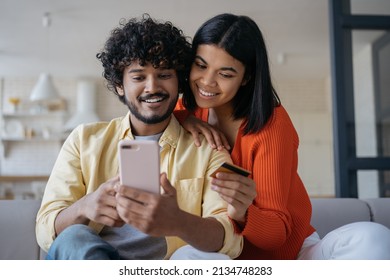 Smiling multiracial couple holding credit card shopping online, ordering food looking at digital screen sitting at cozy home. Happy freelancers receive payment, successful business - Powered by Shutterstock