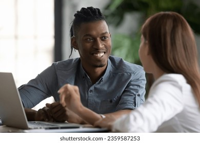 Smiling multiracial coworkers sit at desk in office talk discuss business ideas at meeting together, diverse multiethnic colleagues brainstorm at briefing, cooperate work on laptop, teamwork concept - Shutterstock ID 2359587253