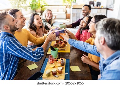 Smiling Multiracial Group Of Young People Having Breakfast, Laughing And Cheering With Hot Drinks Together At Coffee Bar - Diverse Millennial Colleagues Enjoying Meal During Work Break - Focus On Cups