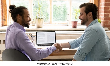 Smiling multiracial male colleagues clients shake hands get acquainted greet at meeting in office. Happy multiethnic businessmen handshake close deal make agreement. Partnership concept. - Shutterstock ID 1916410556
