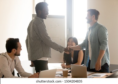 Smiling multiracial male employees stand handshake get acquainted at team meeting in office, happy diverse business partners shake hand greeting or closing deal at briefing, cooperation concept - Shutterstock ID 1504204835