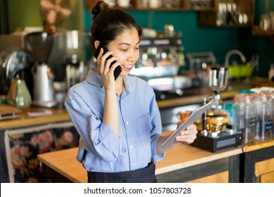 Smiling Multi-tasking Manager Working In Restaurant. Smiling Confident Small Business Owner Talking On Phone And Viewing Notes On Tablet. Cafe Concept