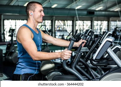 Smiling Muscular Man Using Elliptical Machine At Gym