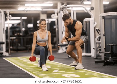 Smiling muscular sportswoman doing lunges with dumbbells in hands with her coach. - Powered by Shutterstock