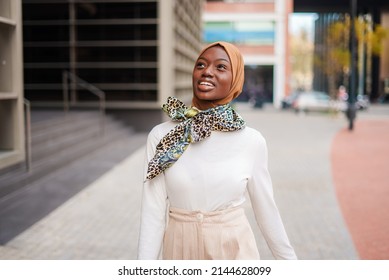 Smiling Muslim black woman in hijab standing near office building