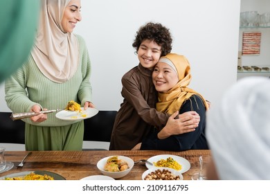 Smiling muslim boy hugging asian grandmother near mom and food at home