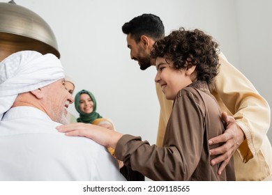 Smiling muslim boy hugging granddad near family at home