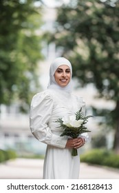 smiling muslim bride with diamond ring on finger holding wedding bouquet