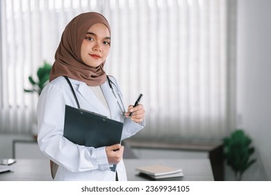 smiling muslim female doctor in brown hijab carrying medical records - Powered by Shutterstock