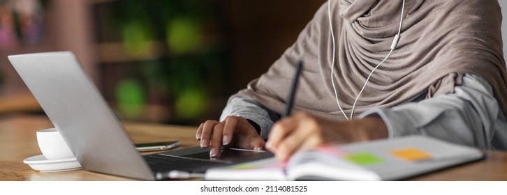 Smiling muslim lady studying online at cafe, using laptop and headset, free space. Joyful female student having online lesson, looking at laptop screen and taking notes, online education concept - Shutterstock ID 2114081525