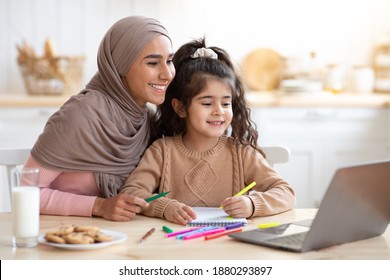 Smiling Muslim Mother And Her Little Daughter Using Laptop In Kitchen Together, Loving Islamic Mom Helping Girl With Online Education And Development Activities, Looking At Computer Screen And Smiling - Powered by Shutterstock