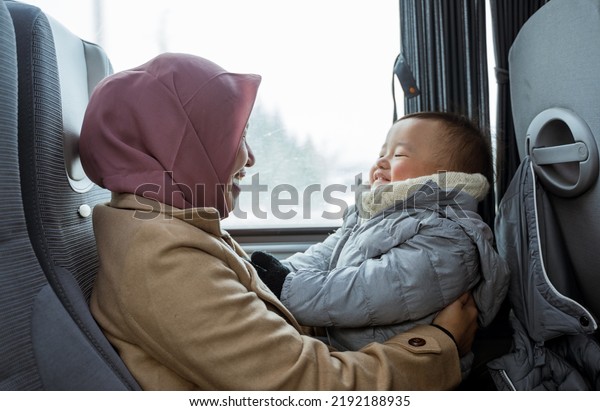 smiling muslim mother and toddler sitting inside\
the bus playing\
together