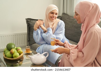 Smiling Muslim Women Drinking Tea And Chatting At Home