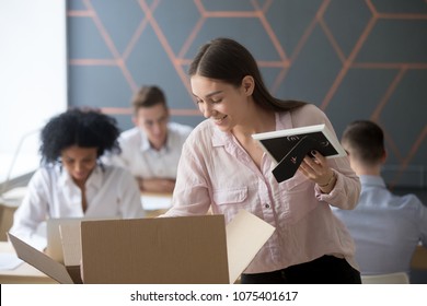 Smiling New Hired Female Employee Unpacking Box With Belongings Holding Framed Picture At Workplace In Shared Office, Happy Intern Or Newcomer Starting Work In Company On First Day Of Job Concept