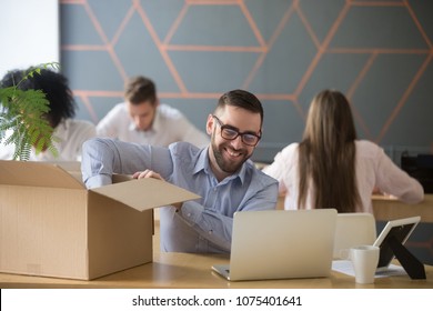 Smiling new male employee unpacking box with belongings at workplace, happy hired office worker newcomer on first working day concept, excited millennial businessman put laptop on desk in coworking - Powered by Shutterstock