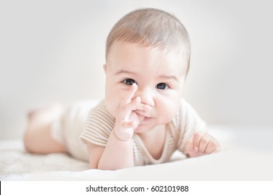 Smiling Newborn Baby Lying On Bed With His Fingers In The Mouth. Teething.