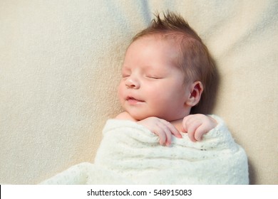Smiling newborn baby with Mohawk hair sleeping in white blanket.