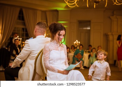 The Smiling Newlyweds Sitting Back To Back On The Chairs In The Restaurant And Playing The Game