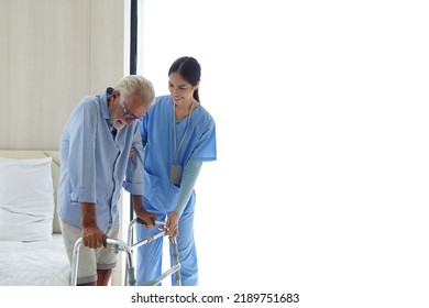 Smiling Nurse Assisting Senior Man To Get Up From Bed. Caring Nurse Supporting Patient While Getting Up From Bed And Move Towards Walker At Home. Helping Elderly Disabled Man Standing Up