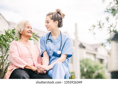 Smiling nurse caregiver holding hand of happy Asian elderly woman outdoor in the park