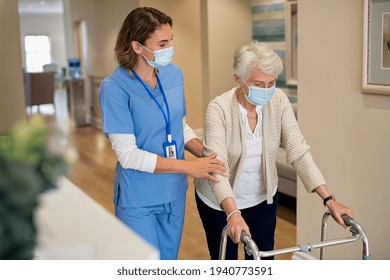 Smiling nurse with face mask helping senior woman to walk around the nursing home with walker. Young lovely nurse helping old woman with surgical mask for safety against covid-19 using a walking frame