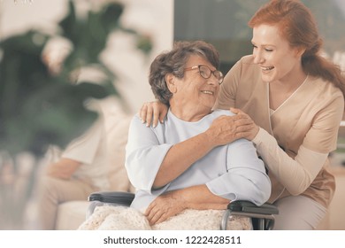 Smiling nurse supporting happy disabled elderly woman in the wheelchair
