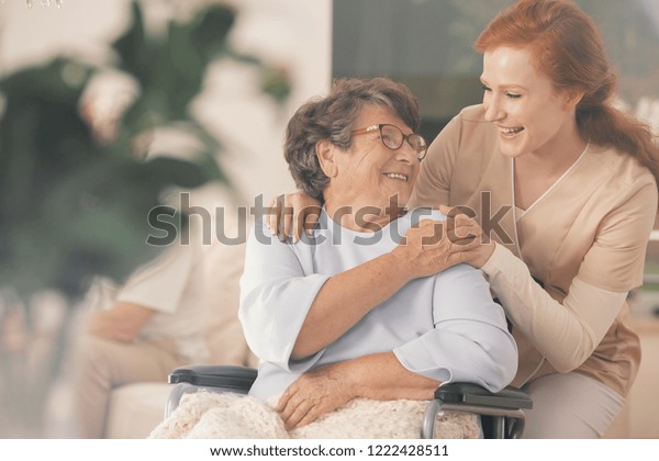 Smiling nurse supporting happy disabled\
elderly woman in the\
wheelchair