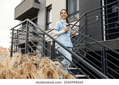 Smiling nurse with tablet and coffee to go in hands descending staircase and rushing to work. - Powered by Shutterstock