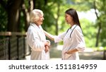 Smiling nurse talking with elderly woman in bathrobe at sanatoria park, relax