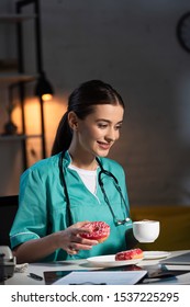 Smiling Nurse In Uniform Holding Donut And Cup During Night Shift