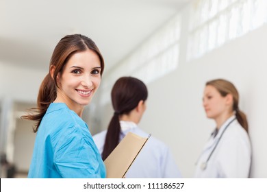 Smiling Nurse  While Standing In A Hallway With A Patient And A Doctor In A Hallway