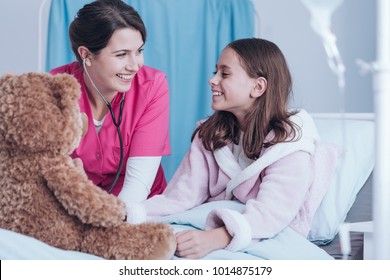 Smiling Nurse And Young Patient Examining A Teddy Bear In The Clinic