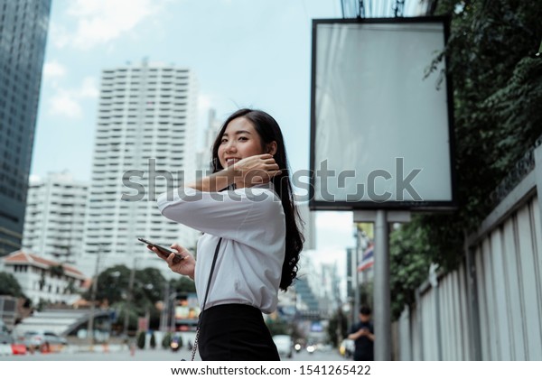 Smiling office girl using mobile phone on\
the city street close to huge banner\
pole.