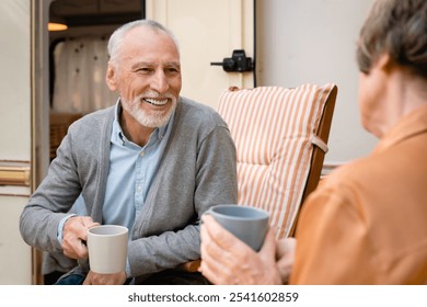 Smiling old elderly senior couple spouses talking drinking tea while driving camper van trailer, caravanning outdoors, doing eco-tourism together - Powered by Shutterstock